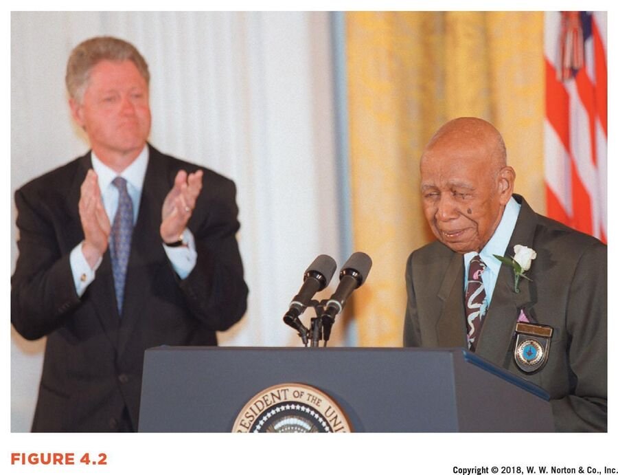 Tuskegee survivor Herman Shaw speaks at a White House podium in 1997 as President Bill Clinton applauds.