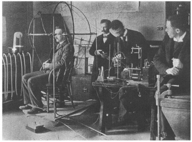 Early twentieth-century psychology laboratory: a seated man wired to apparatus while researchers observe.