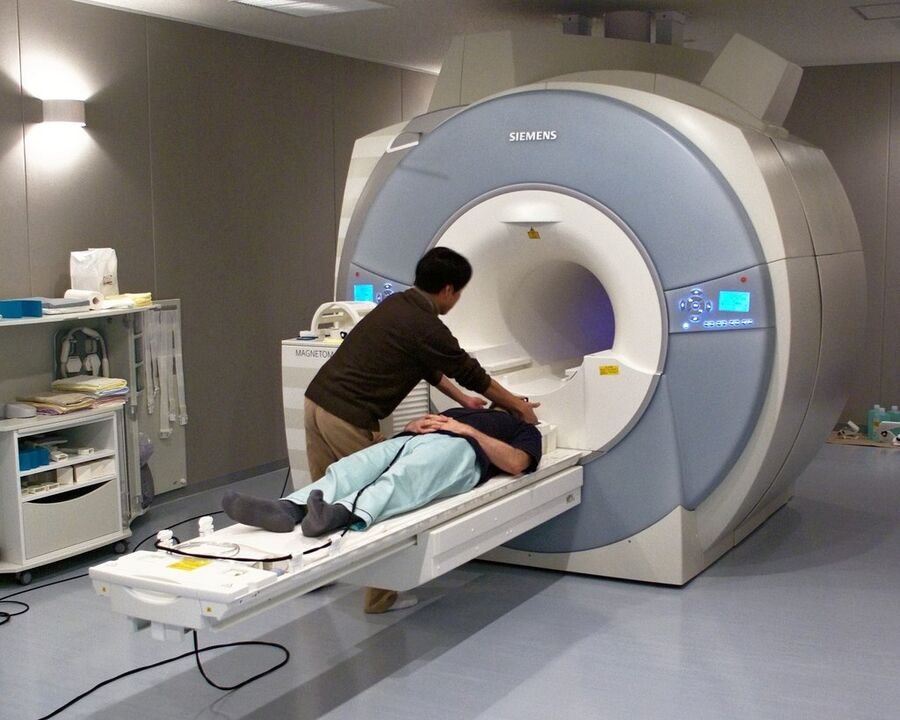 A person lying on the bed of an MRI scanner while a technician assists.