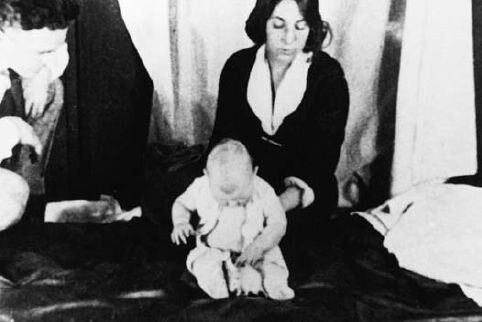 Black-and-white photo of the infant 'Little Albert' sitting calmly between two researchers.