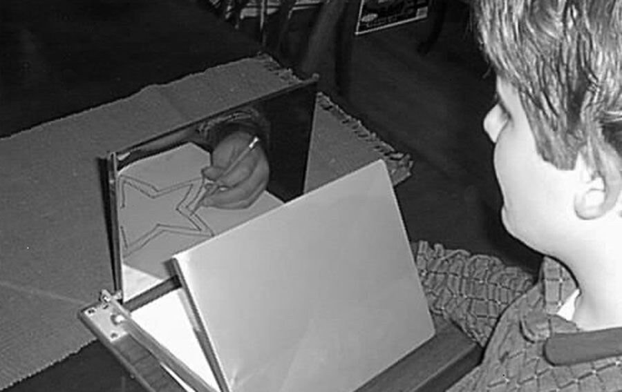 A young person tracing a star shape while looking only at its reflection in a mirror, their hand hidden behind a shield.