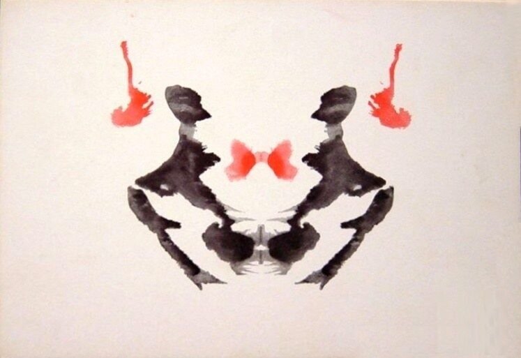 A symmetrical Rorschach inkblot in black with small red accents.