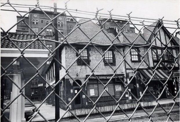 A black-and-white photo of the Kew Gardens street and buildings where the Genovese attack took place, seen through a chain-link fence.