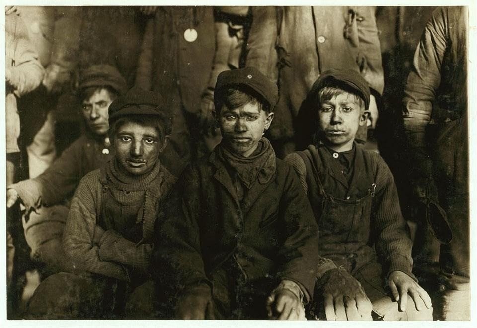 Several young coal-mine workers seated together, faces darkened with coal dust.