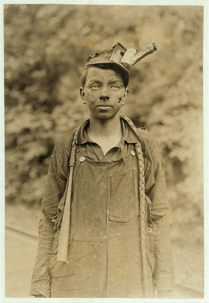 Sepia portrait of a young miner in overalls with a lamp on his cap.