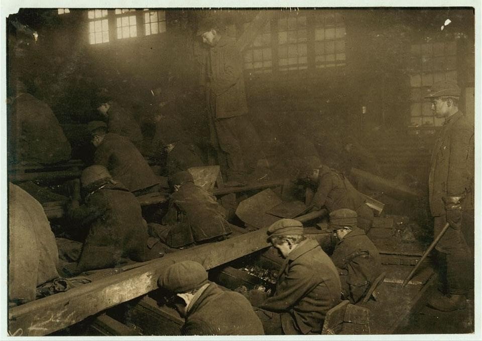Boys hunched over chutes sorting coal inside a dark breaker building.