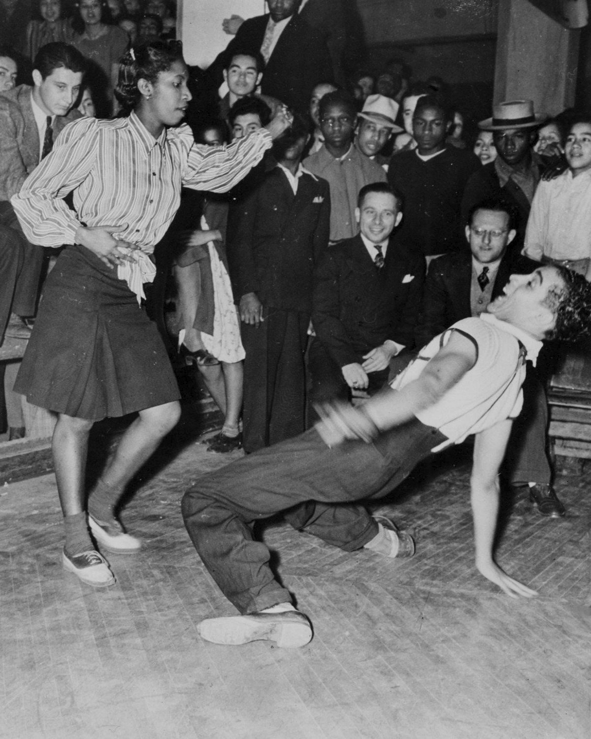 Teenagers jitterbug dancing in the 1940s while others watch.